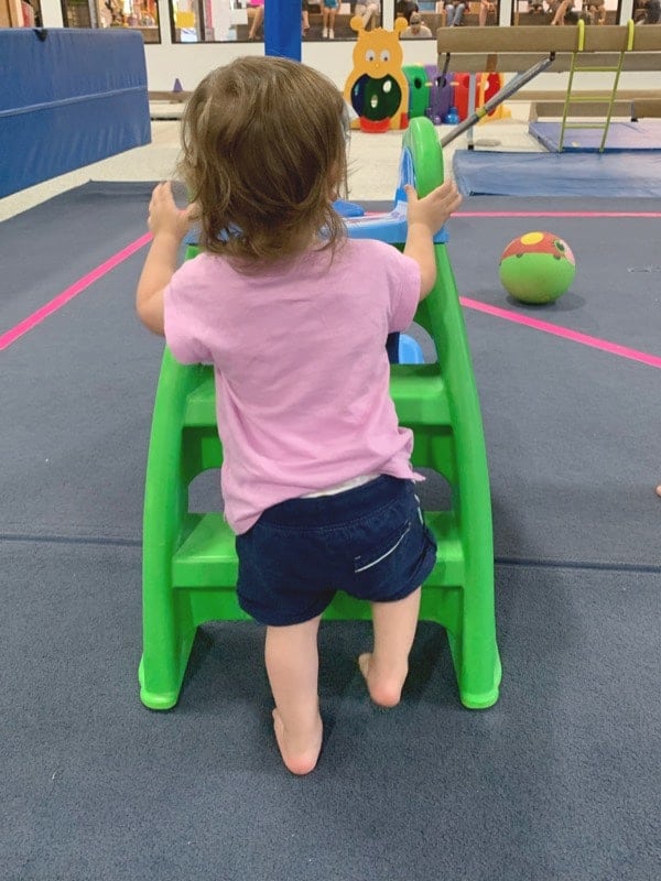 A toddler in a pink shirt climbing a small green and blue plastic slide