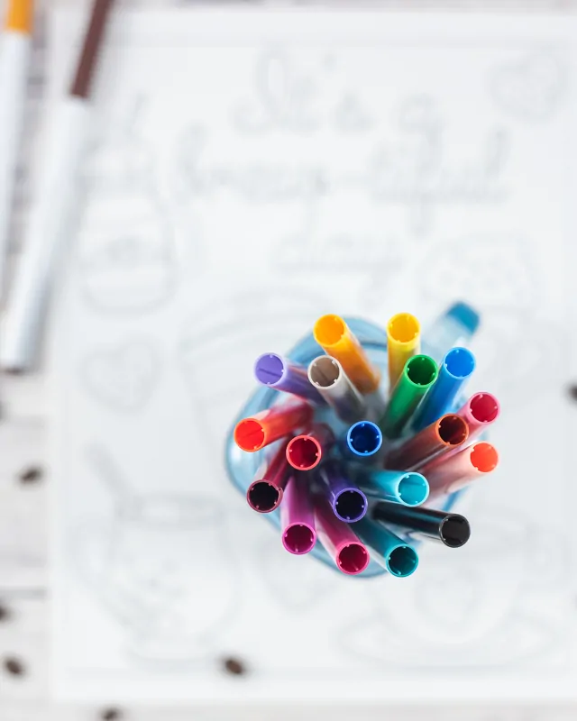 A top down view of a jar of Crayola super tip markers sitting on an out of focus coloring page