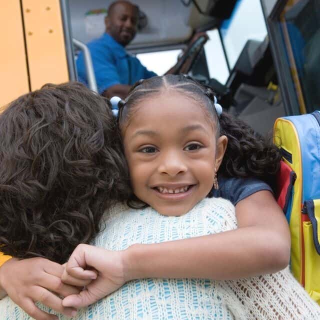 smiling girl hugging mom by school bus