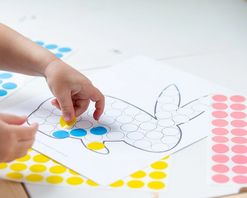 A young child's hand placing a round yellow sticker on a dot marker printable with a bunny.