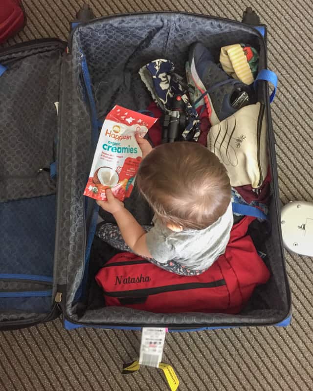 baby sitting in luggage playing with food