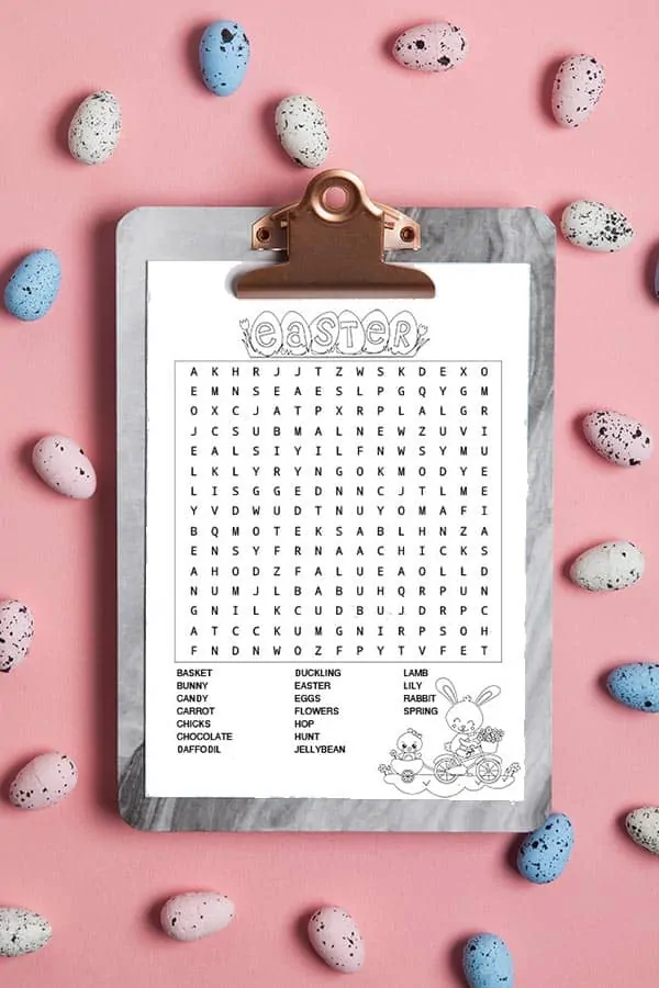 An Easter word search on a grey marble clipboard. The clipper is on a pink background and surrounded by speckled Easter eggs. 