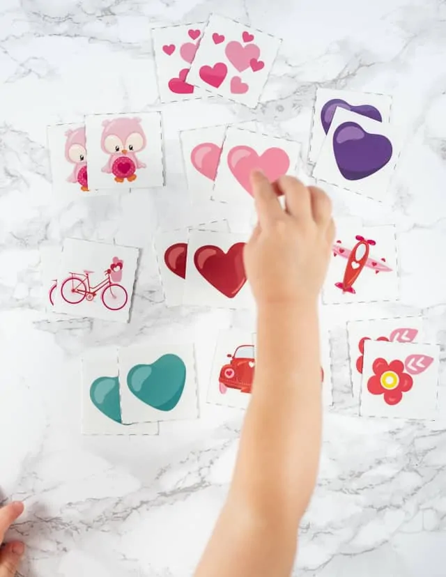 A toddler's hand reaching for a pink heart in a set of Valentine's Day matching game cards