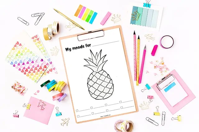 Printable pineapple mood tracker on a clipboard surrounded by pink and tea stationary and office supplies
