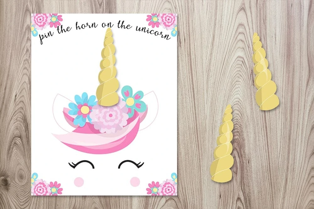 free printable pin the horn on the unicorn poster with three horns on a wood background