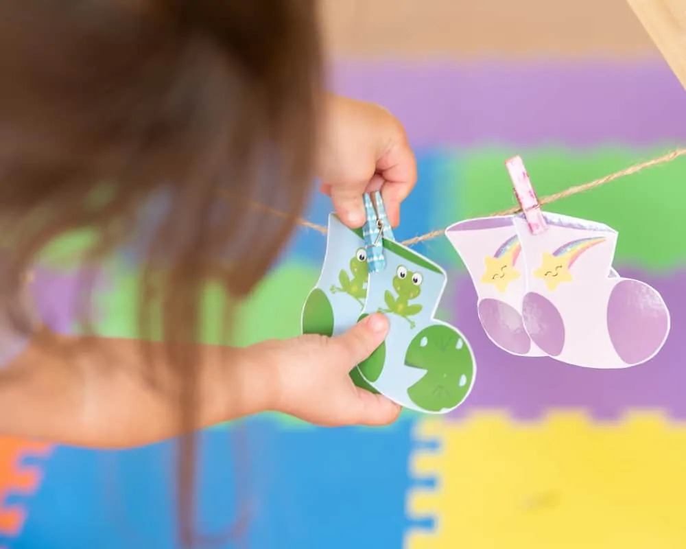 a toddler playing with a pair of printable socks for a matching game. She is unclipping a small clothespin holding them on a line.