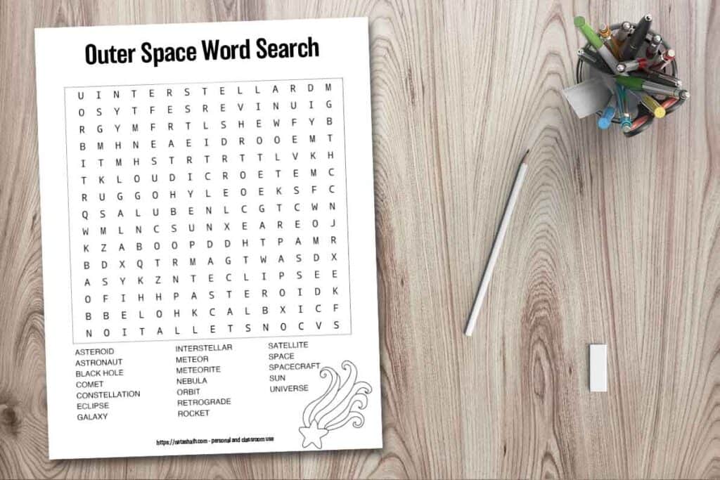 Free printable space word search for kids with words hidden forwards and adults and older children. It has a shooting star to color and 19 space themed words to find. It is shown on a wood background with a pen cup, pencil, and eraser.