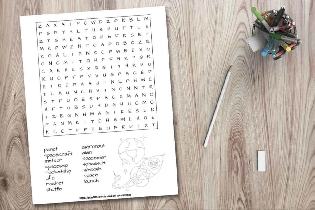 Free printable space word search for kids with words hidden forwards and on straight lines. The word search also has a rocket and planet to color. It is shown on a wood background with a pen cup, pencil, and eraser.
