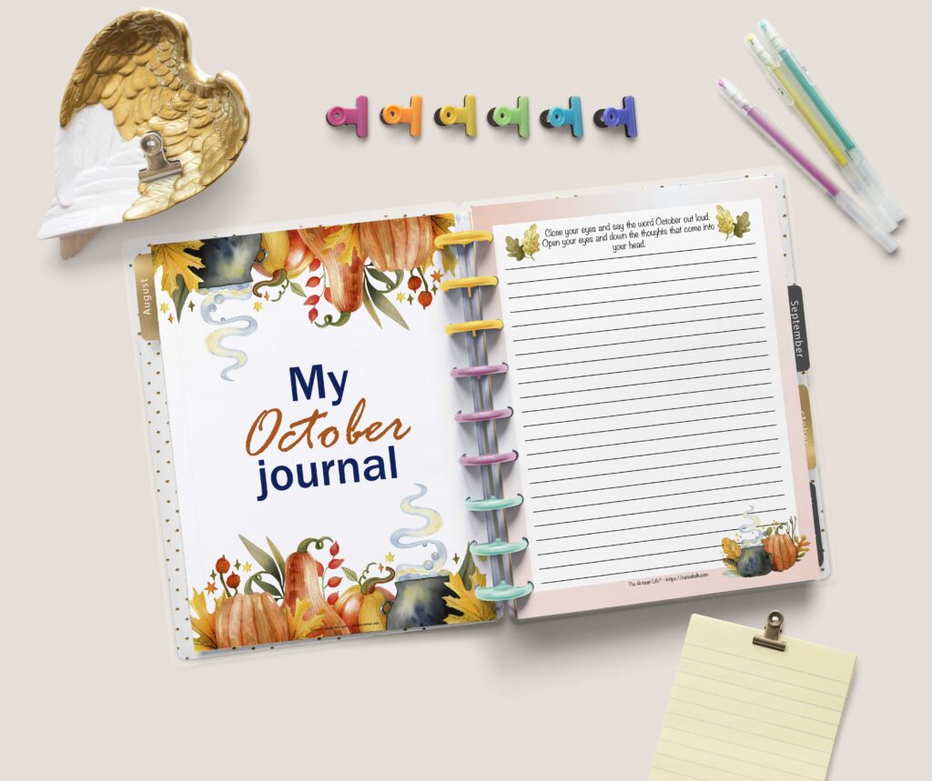 A flat lay of an open Happy Planner Classic with a page "My October Journal" with watercolor pumpkins and leaves on the left and a lined journal page on the right. There are colorful binder clips, a tray shaped like gilded wings, and three gel pens above the planner. Below the planner is a yellow note sheet with a gold binder clip.
