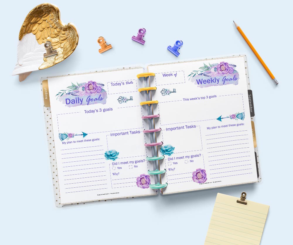 A flatly scene of a Happy Planner classic planner open to daily and weekly goal setting planner pages. The pages feature purple and pink watercolor anemone flowers and boho arrows. The planner is surrounded by stationary supplies.