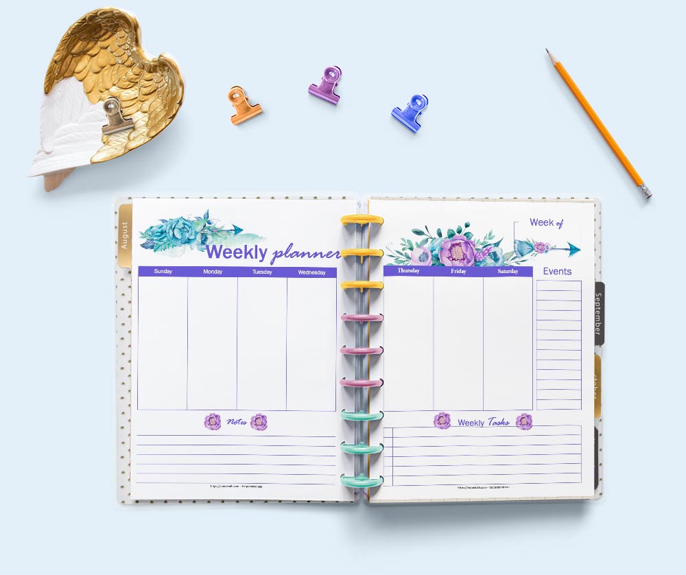 A flatly scene of a Happy Planner classic planner open to a two page spread of weekly planner pages. The pages feature purple and pink watercolor anemone flowers and boho arrows. The planner is surrounded by stationary supplies.