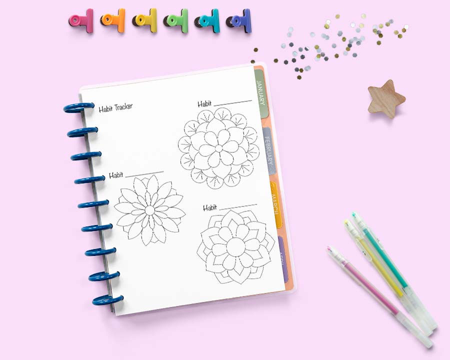 an open disk bound Happy Planner on a pink surface with colorful binder clips and gel pens. The planner is open to a page with three small circular trackers shaped like geometric flowers.