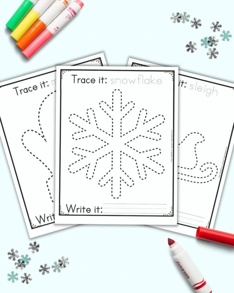 Three free printable winter themed tracing images for preschoolers and kindergarteners. The front and center page has a dotted snowflake to trace. It has the caption "Trace it: snowflake" on top and "write it" with a blank line for writing below the snowflake. Behind the snowflake are a mitten and a sleigh to trace on separate pages. The printables are on a blue background with snowflake confetti and brightly colored children's markers. 