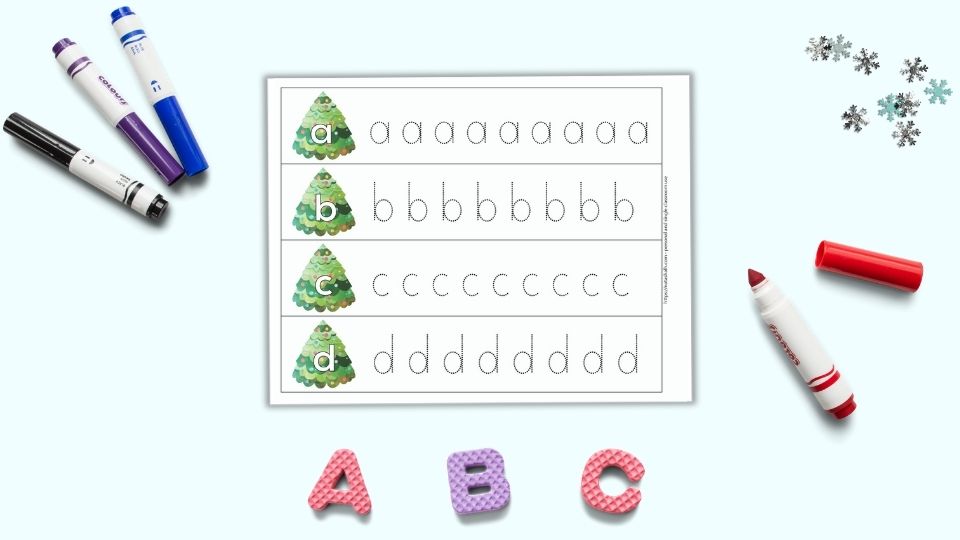 A preview of one printable alphabet tracing page for preschoolers. The page has four rows with one letter per line - a, b, c, d" A large bubble letter is on a Christmas tree on the left. To the right is a line of dotted letters to trace. The pages are on a light blue surface. Below the pages are foam letters "A B C." There are four colorful children's markers around the printable pages.