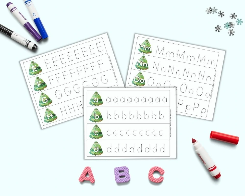 A preview of three printable alphabet tracing pages for preschoolers. Each page has four rows with one letter per line - a, b, c, etc. A large bubble letter is on a Christmas tree on the left. To the right is a line of dotted letters to trace. The pages are on a light blue surface. Below the pages are foam letters "A B C." There are four colorful children's markers around the printable pages.