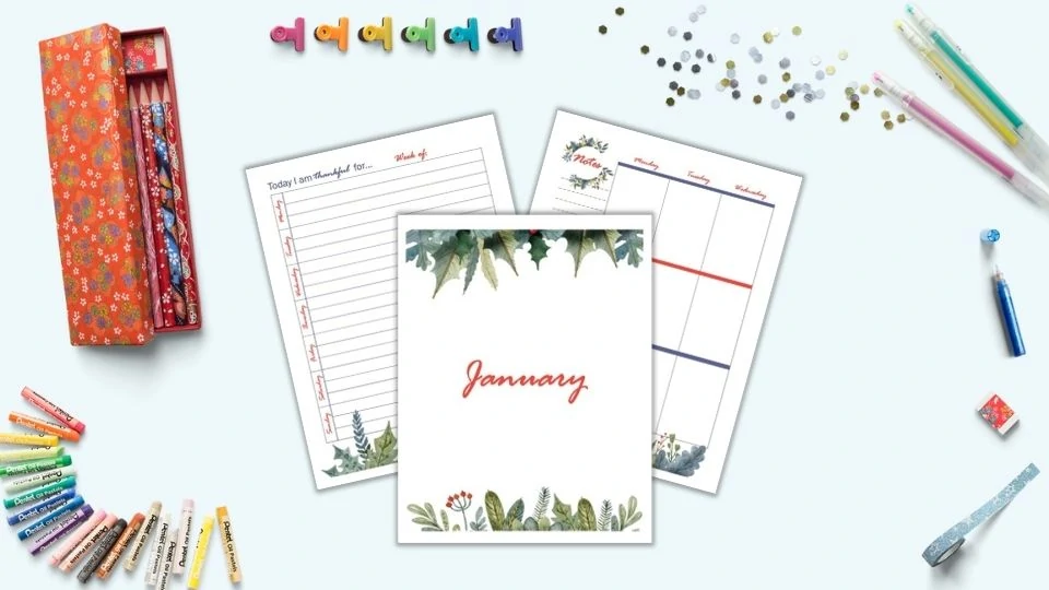 A preview of three printable January planner pages including a gratitude journal page, cover page, and first page of a vertical weekly layout. The pages are on a blue surface surrounded y desk supplies including gel pens, colorful binder clips, oil pastels, and a red pencil case.