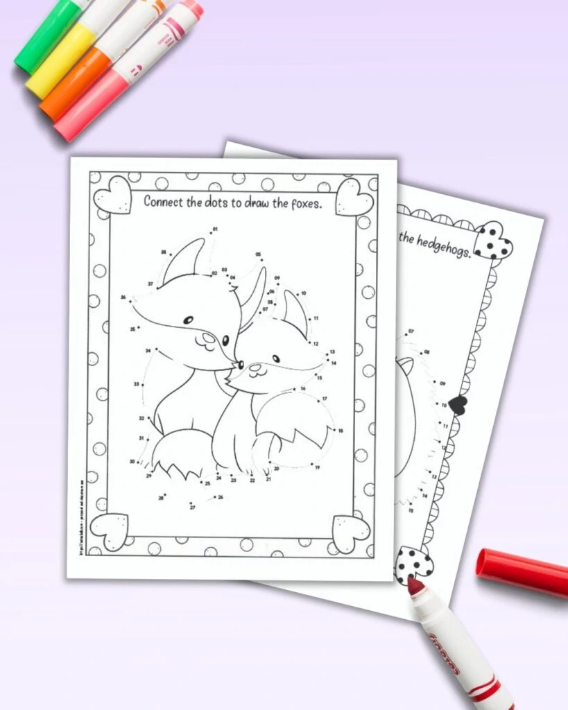 A flatlay preview of two printable dot to dot pages with doodle heart frames. The top page has two cute foxes cuddling. The pages are shown with colorful children's markers.