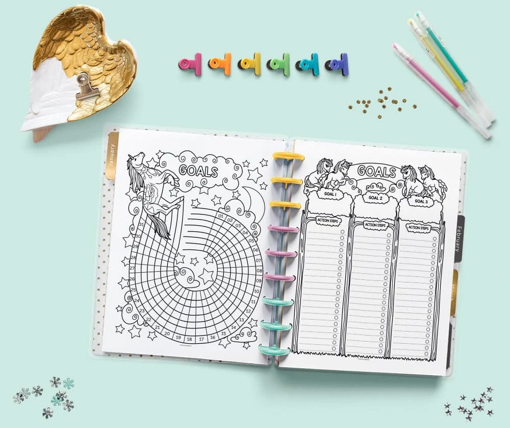An open Happy Planner Classic with unicorn themed goal tracer and goal planner pages. The planner is on a teal surface with gel pens and colorful binder clips.