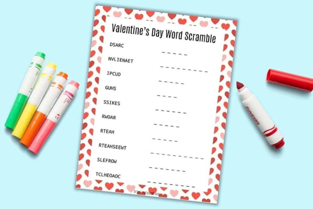 a printable Valentine's Day word scramble for children with a red and pink heart border. The page is on a light blue background with six colorful children's markers. The red marker is open.