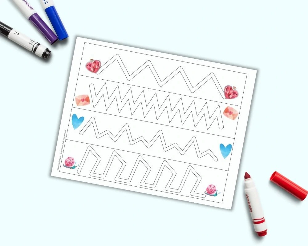 A printable trace in the path worksheet with zigzag lines to trace inside of and Valentine's Day watercolor images. The page is on a light blue background with colorful child's markers.