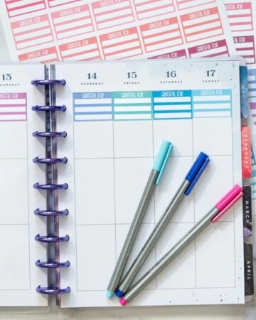 a top down photo of an open Happy Planner with a row of printable colorful gratitude stickers across the top of each weekly box.