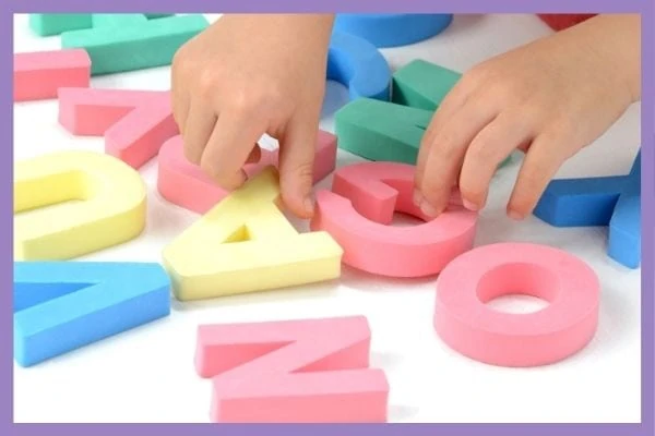 A close up of a child's hands playing with colorful foam letters