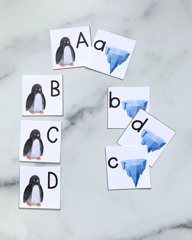 Eight cut out alphabet tiles. On the left are a-d in uppercase letters with a penguin on each card. On the right are letters a-c in lowercase with an iceberg on each card.