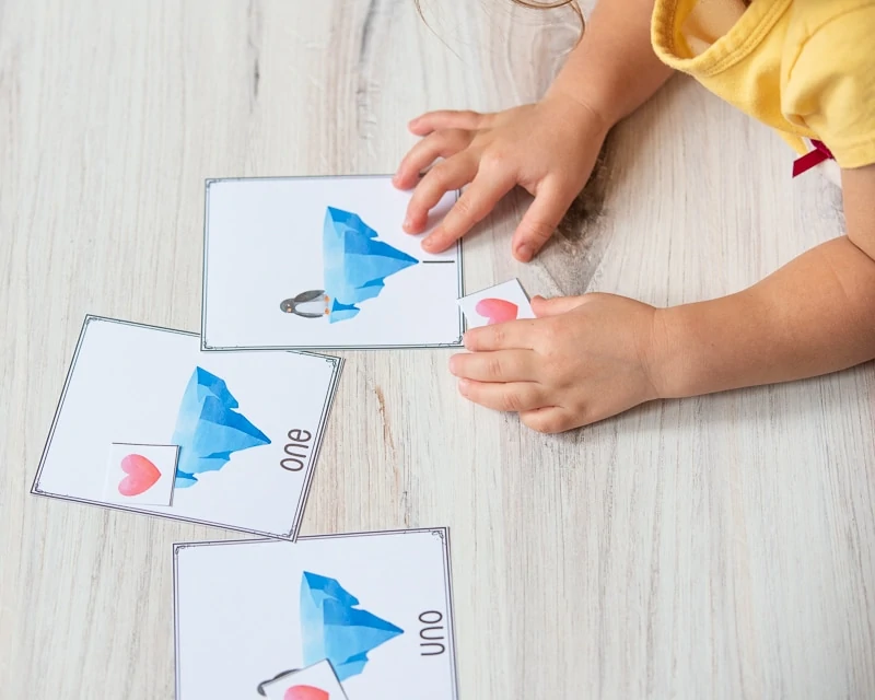 A child's hand pointing at the number "1" on the bottom of a card with an iceberg and a penguin on it.