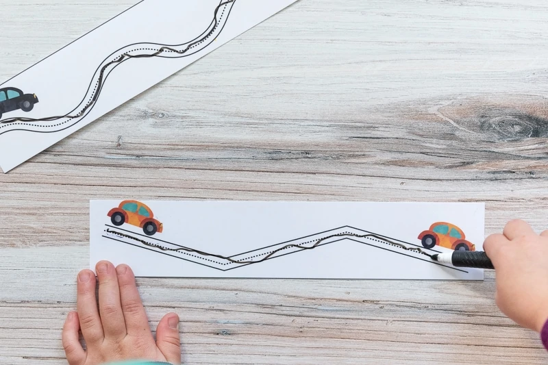 A top down view of a child's hands using a dry erase marker to race inside of a zig-zag path