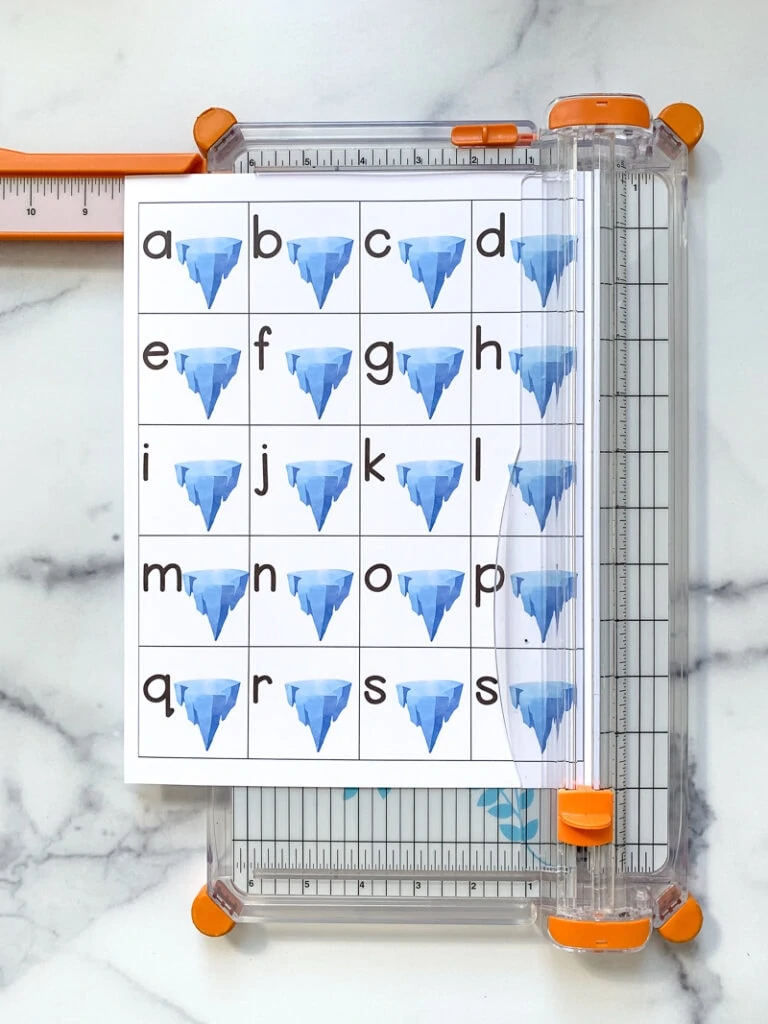 A paper trimmer trimming the right margin off a page with 20 tiles. Each tile as a lowercase letter a-t and an iceberg.