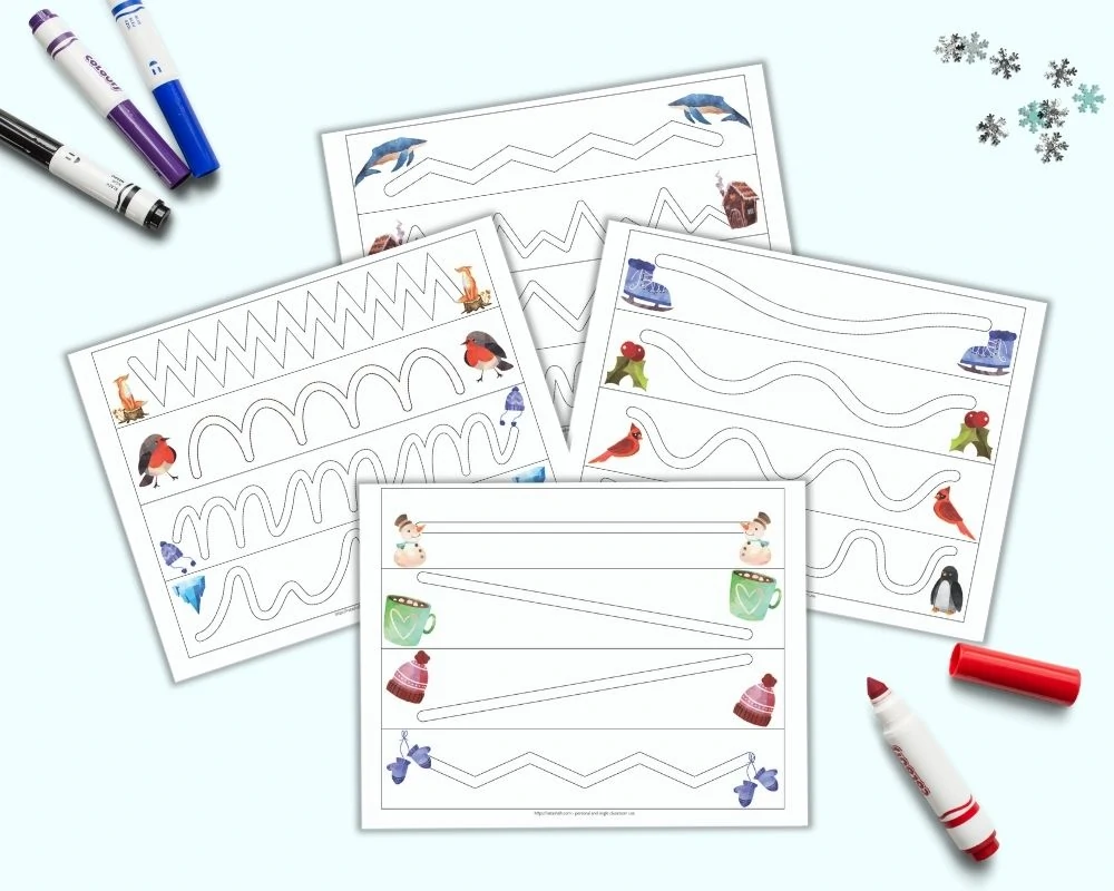 a flatlay mockup of four printable trace in the path worksheets for preschoolers. Each page has four paths to trace inside. A watercolor winter-related clip art image is on either side of each path. The pages are on a light blue background with four colorful child's markers and a few pieces of blue and silver snowflake confetti. 