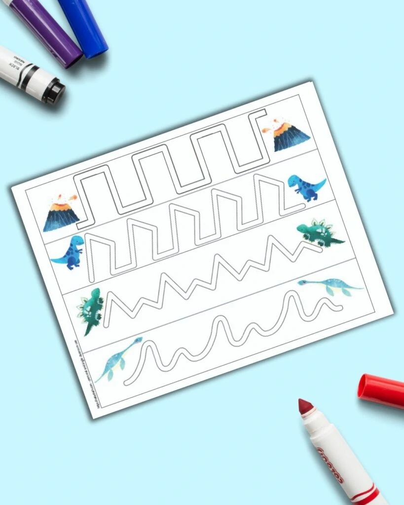 A preview of a dinosaur themed trace in the path fine motor practice page for preschoolers. The page is on a blue surface with colorful children's crayons. 
