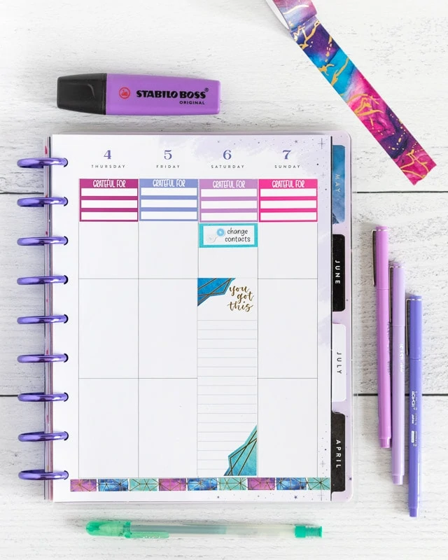 A top down photo of a Happy Planner.  A gratitude journal sticker is across the top of each day on the right hand side of a weekly vertical layout page. A blue "change contacts" sticker is on Saturday. There are purple pens, highlighters, and washi tape around the planner. 