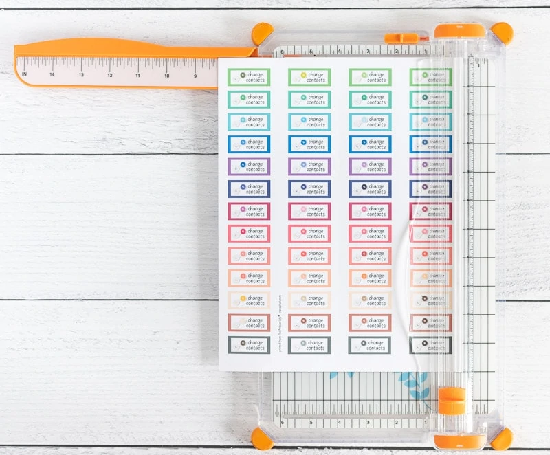 A sheet of colorful "change contacts" reminder stickers for Happy Planner on top of a paper cutter.