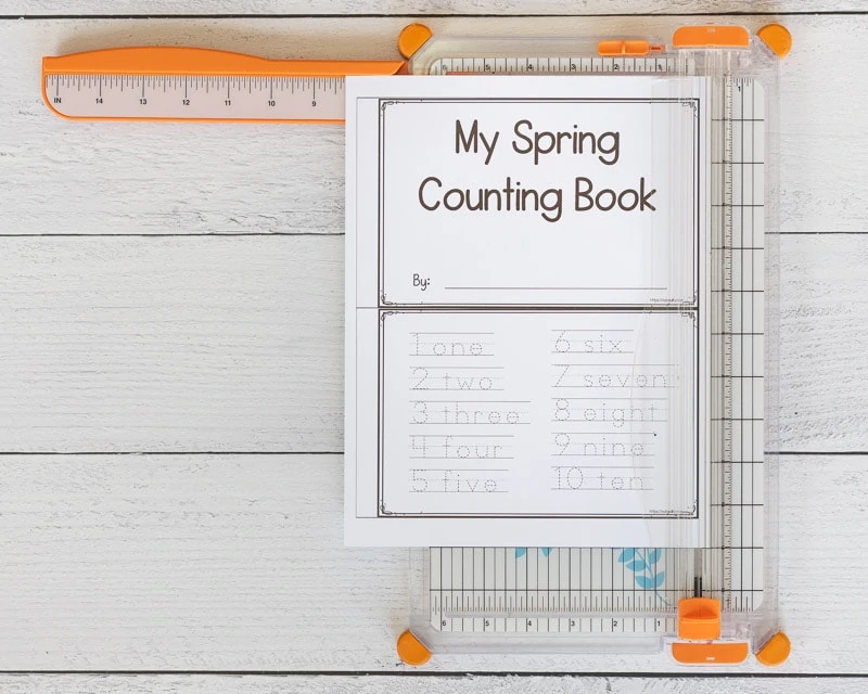A page on a paper cutter. The page has two sheets of an emergent reader printable for preschoolers to cut apart. The top page reads "My spring counting book" and the bottom of he page has numbers 1-10 in a dotted font to trace. 