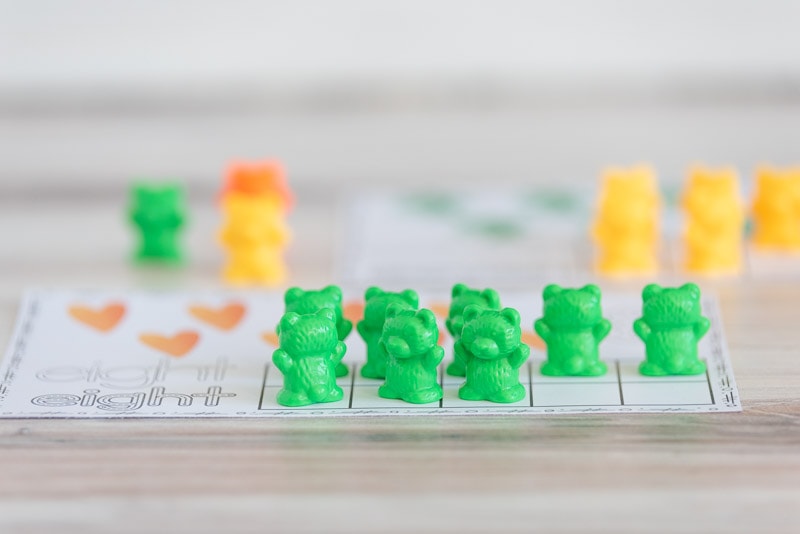An image of green counting bears on a ten frame card with eight orange hearts.