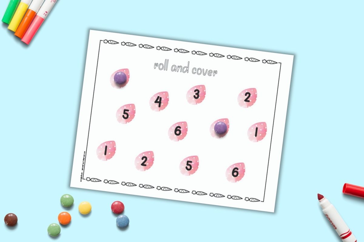 A free printable Easter roll and cover mat for preschoolers. The mat has 12 pink Easter eggs and each egg has a number 1-6 printed on it. Two numbers are covered with round purple candies. More candies are on a blue surface beside the mat.