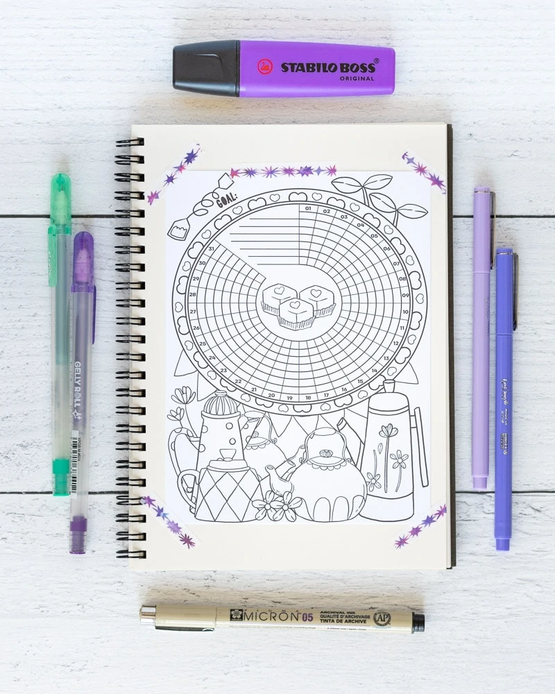 A tea themed habit and goals tracker taped into a spiral notebook. The notebook is on a white wood surface with purple pens and a purple highlighter.