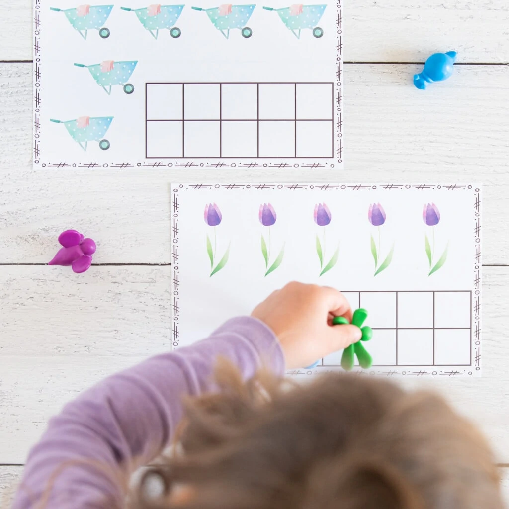 A top down image of a young child wearing a purple shirt placing a green plastic dragonfly on a spring ten frame printable with five watercolor tulips.
