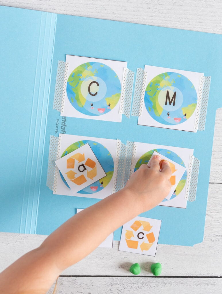 A young child's arm reaching to press a lowercase letter t card with a recycling symbol on it on top of a card with the planet earth and an uppercase letter T on it
