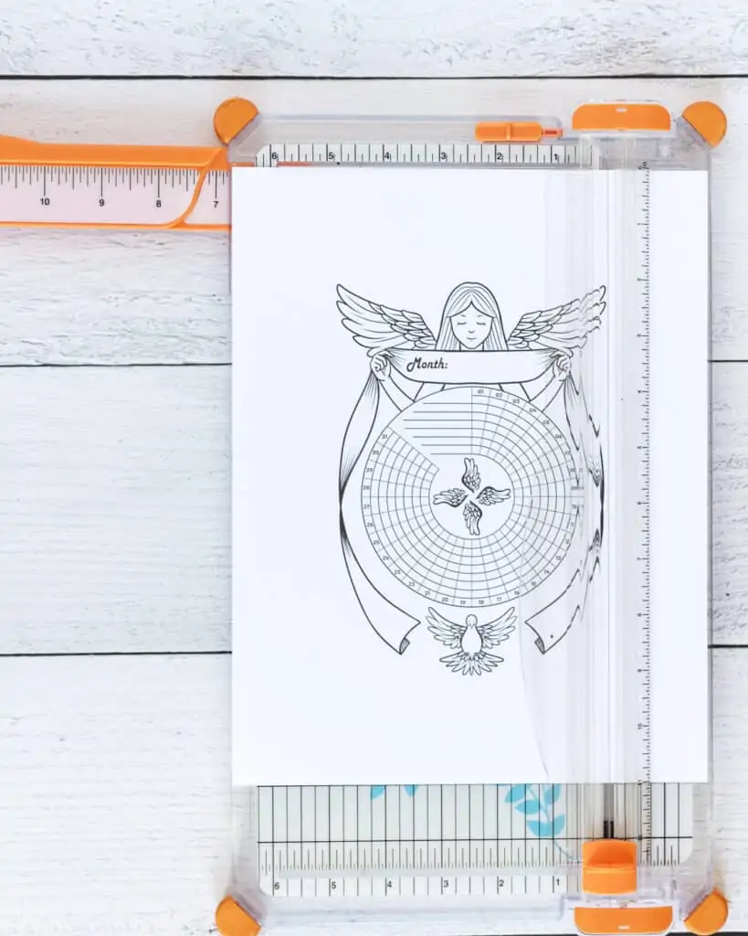 A printed habit tracker with a guardian angel and a dove. The page is on an orange paper trimmer.