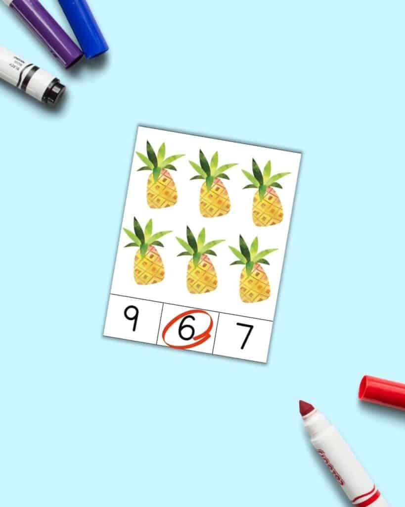A summer theme count and clip card with six watercolor pineapples and three numbers across the bottom - 9, 6, 7. The 6 is circled in red.