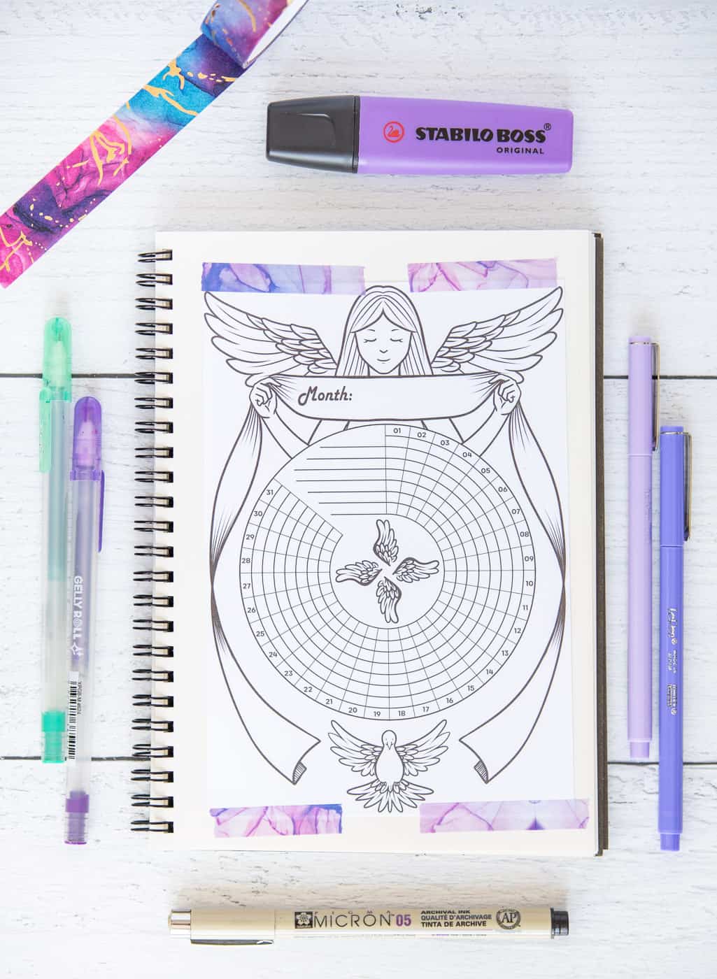 A printed angel themed habit tracker taped to a small spiral notebook with purple marbled washi tape.