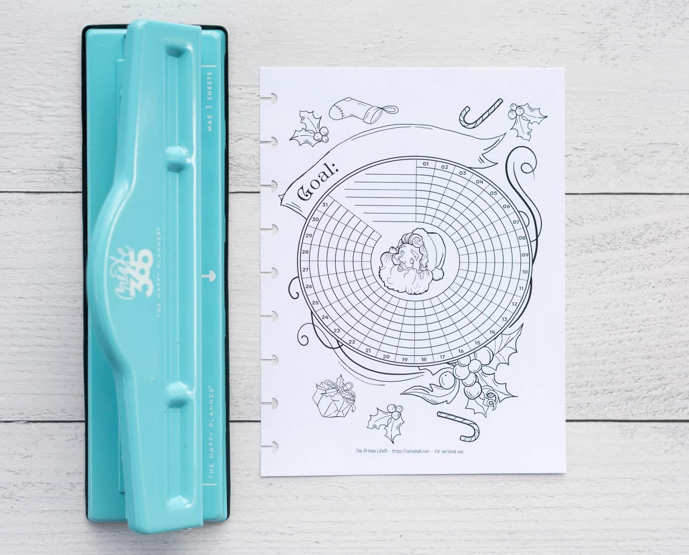 A printable Santa habit tracker with holes punched for a Happy Planner Classic next to a MAMBI hole punch.