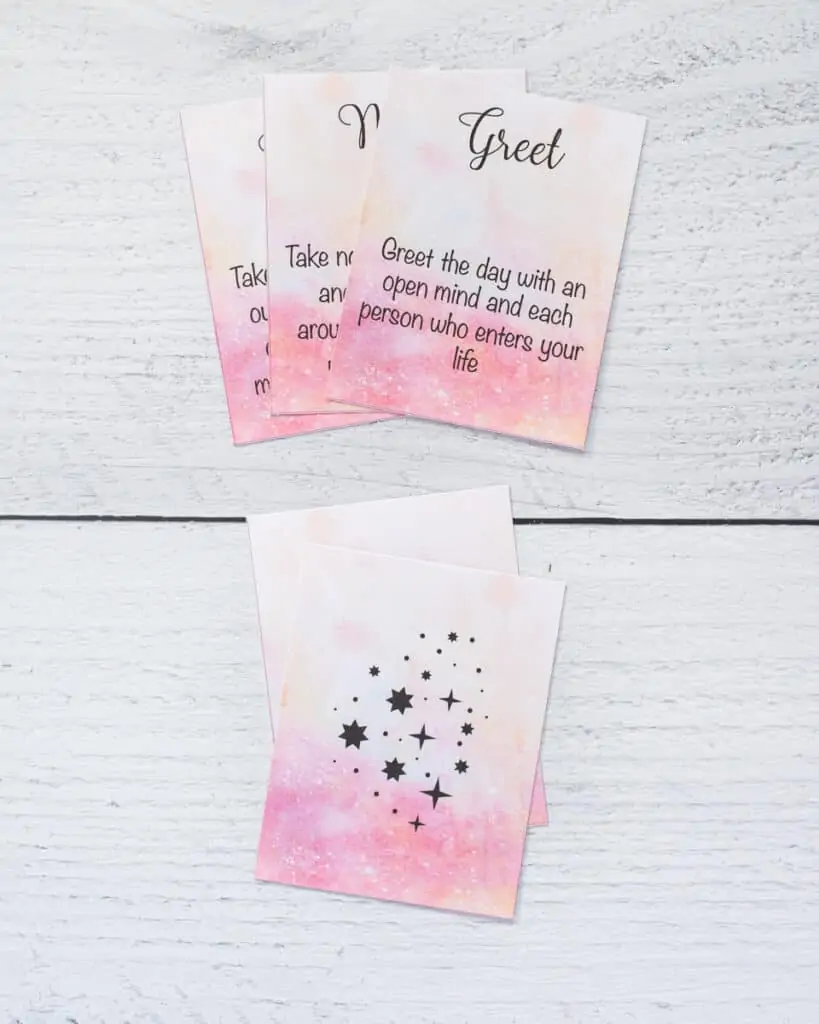 A preview of printed word of the day oracle cards. On top are there cards and below are the back sides of two cards with a pink watercolor background and black stars.