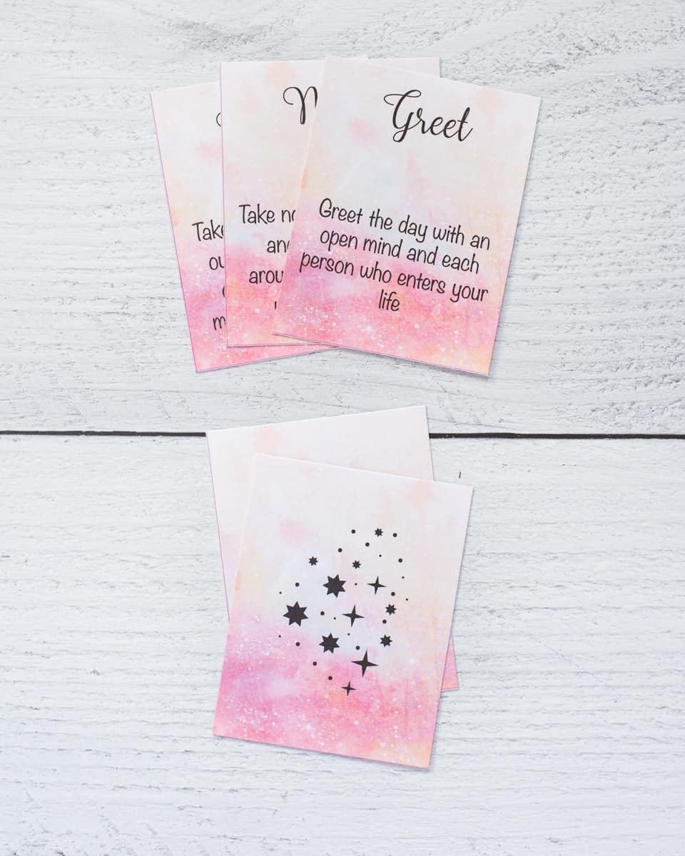 A preview of printed word of the day oracle cards. On top are there cards and below are the back sides of two cards with a pink watercolor background and black stars.