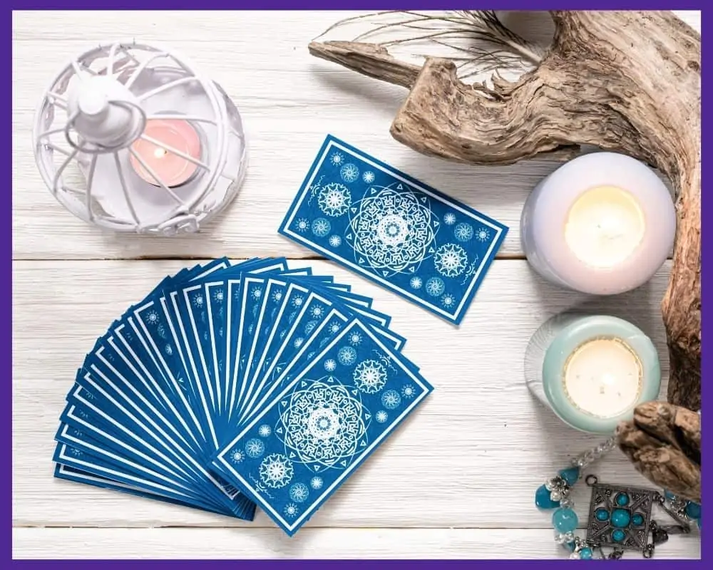 An image with a fan of blue backed tarot cards on a white wood table next to candles and a turquoise necklace
