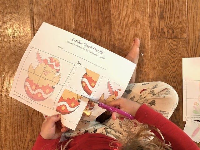 A top down image of a young child using pink scissors to cut out an Easter chick cut and paste puzzle