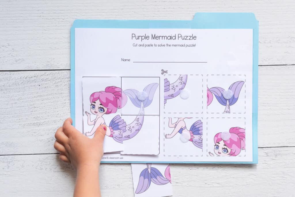 A child's hand solving a purple four piece mermaid puzzle as a file folder game