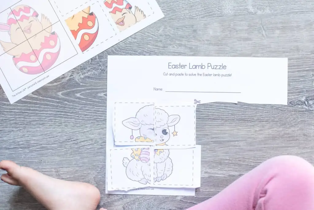A child sitting with a completed cut and paste four part puzzle with an Easter lamb. A puzzle with an Easter chick is visible in the top left.